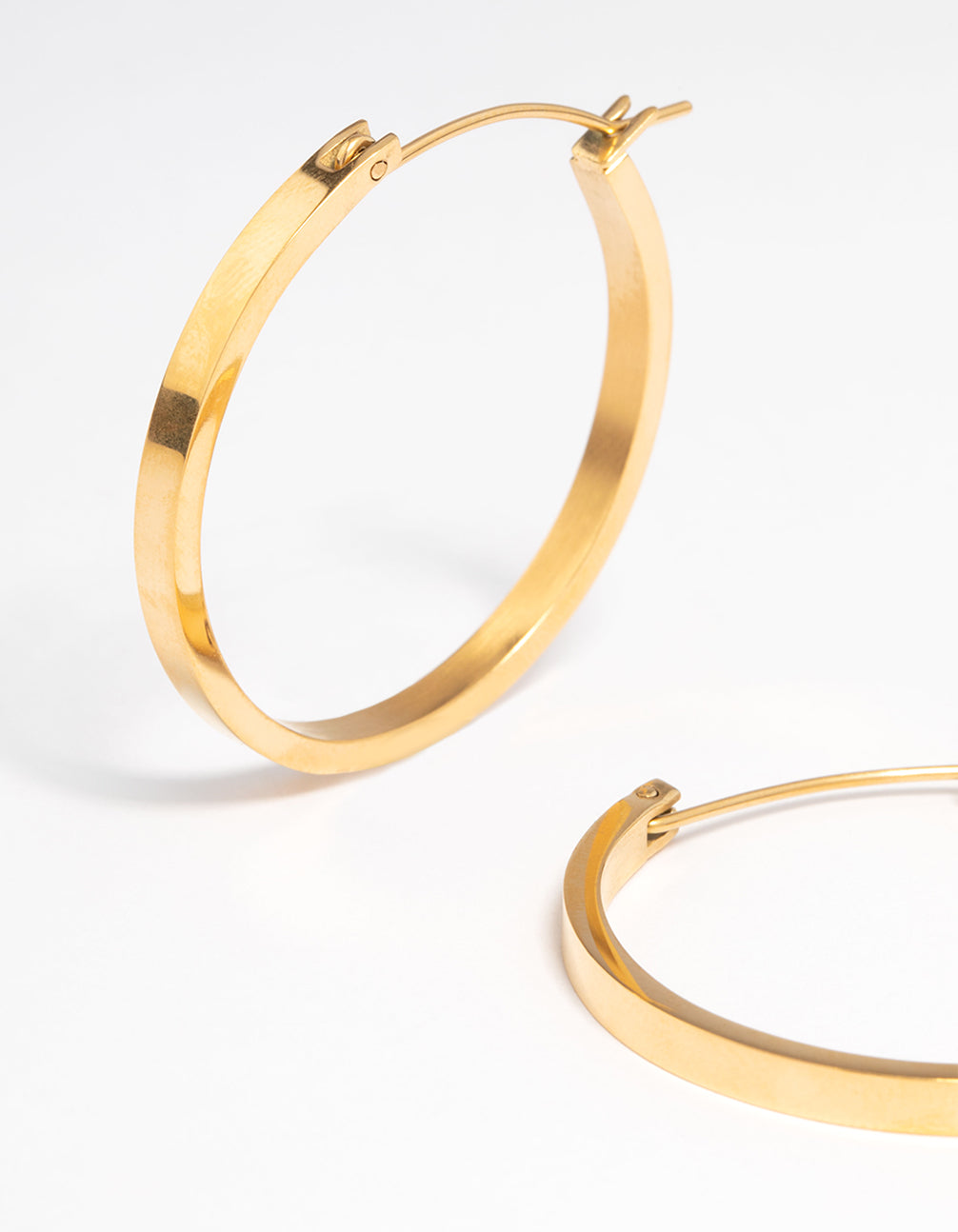 Highlighting waterproof medium flat hoop earrings with gold plated stainless steel construction and hoop closure close up view