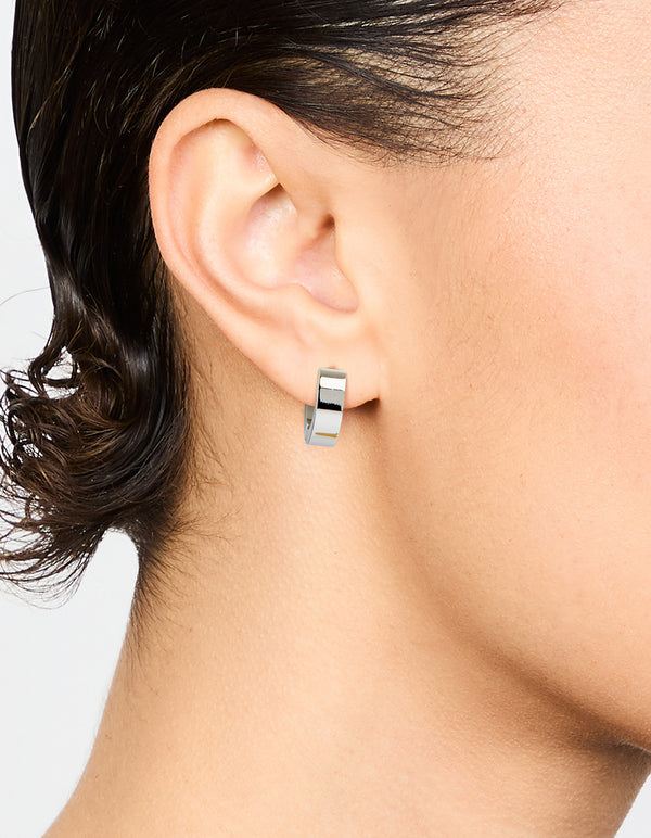 Featuring waterproof stainless steel wide huggie earrings in silver on ear view