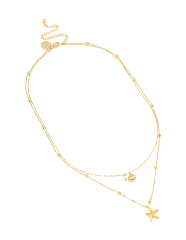 Highlighting a waterproof gold plated stainless steel layered necklace featuring balls, ocean-inspired shell and star charms in gold front view