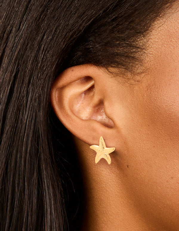 Featuring waterproof gold plated stainless steel textured starfish stud earrings with ocean-inspired design on ear view