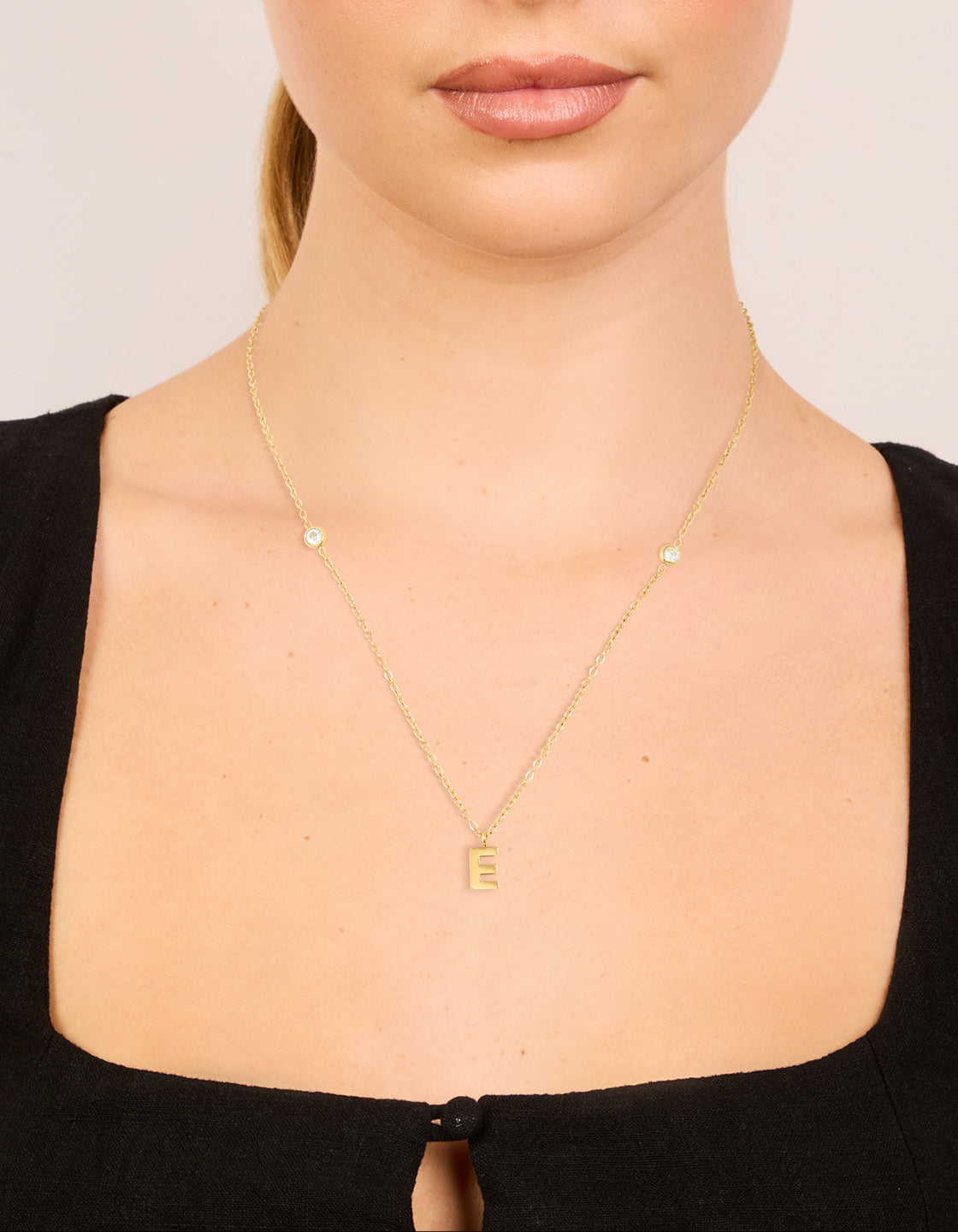 Showcasing a waterproof pendant necklace with letter E initial in gold plated stainless steel featuring dainty design on neck view