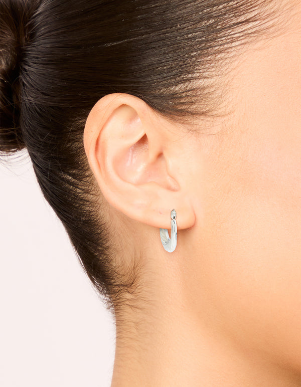 Featuring waterproof textured stainless steel oval hoop earrings in silver on ear view