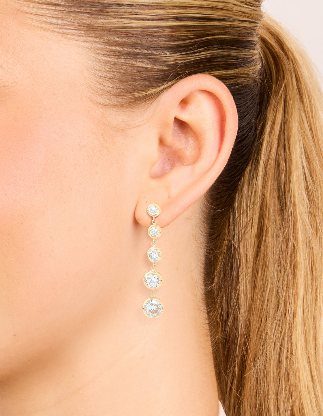 Showcasing waterproof graduating 5-bezel earrings crafted from stainless steel with cubic zirconia in a gold plated finish on ear view