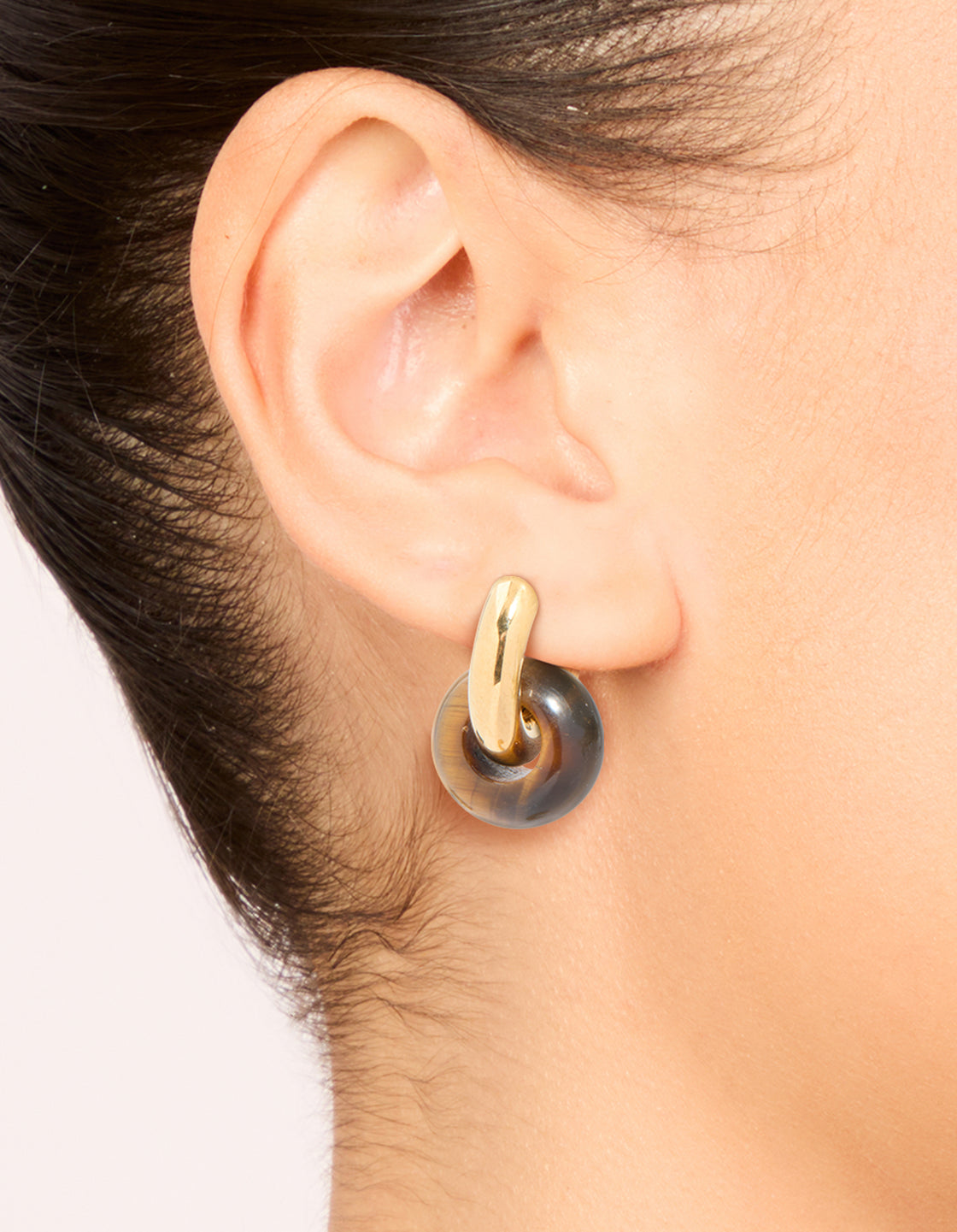Showcasing dainty huggie earrings in waterproof gold plated stainless steel and semi precious tiger's eye stone on ear view