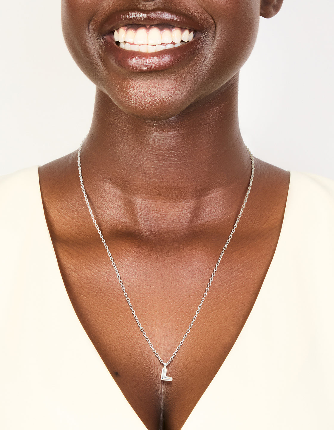 Featuring a waterproof mini bubble letter L necklace with initial pendant in stainless steel silver and dainty design on neck view