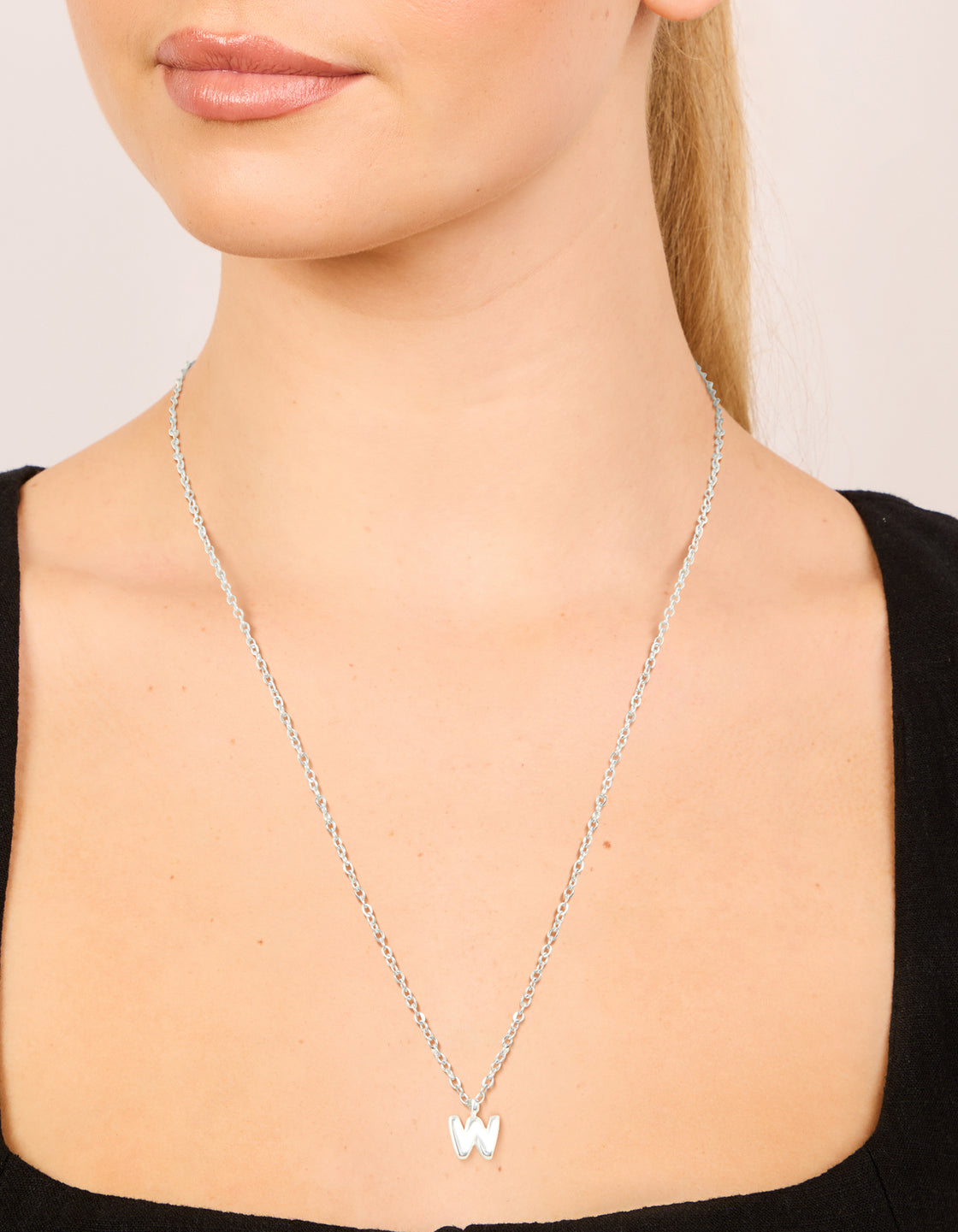 Elegant waterproof stainless steel mini bubble letter W necklace pendant in silver on neck view