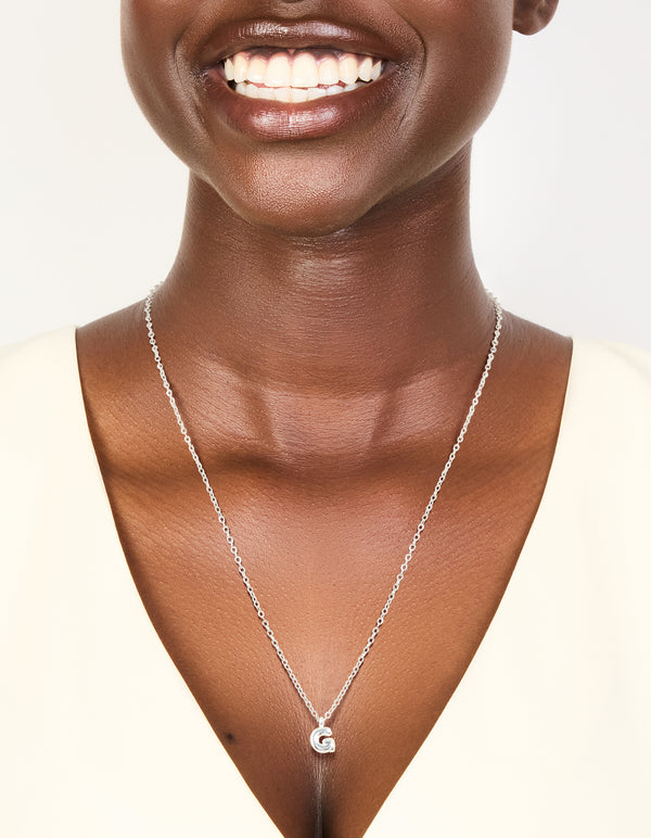 Featuring a waterproof stainless steel mini bubble letter G necklace with charm initials pendant in silver on neck view