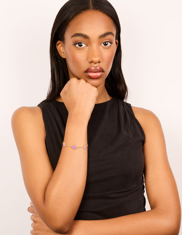 Featuring waterproof gold plated stainless steel, this light purple petal flower charm bracelet in plum on model view