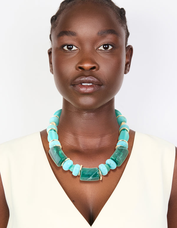 A statement aqua acrylic beaded necklace crafted with turquoise square and round elements separated by gold accents on model view