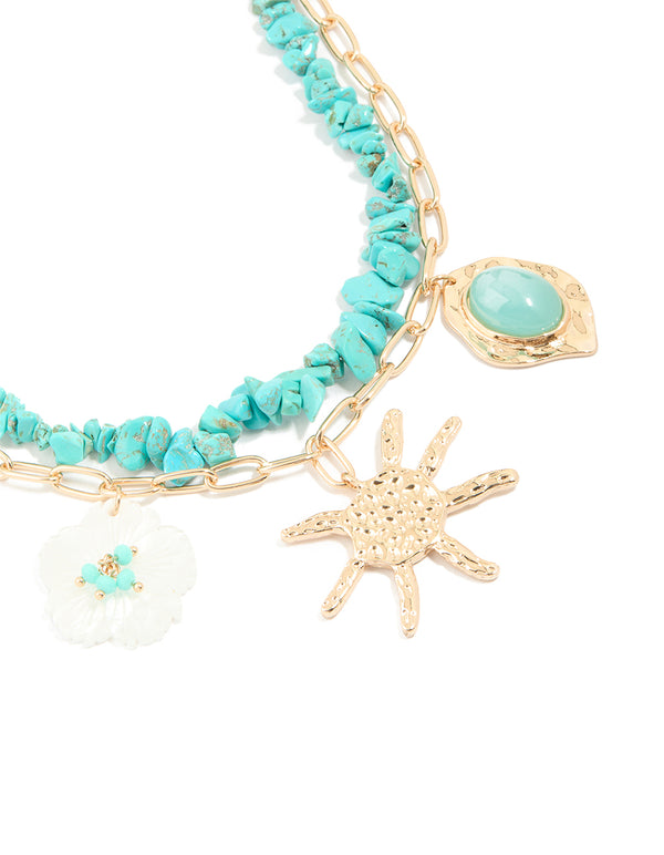 Showcasing a layered necklace with beaded turquoise, floral detail, ocean-inspired and charms in gold close up view