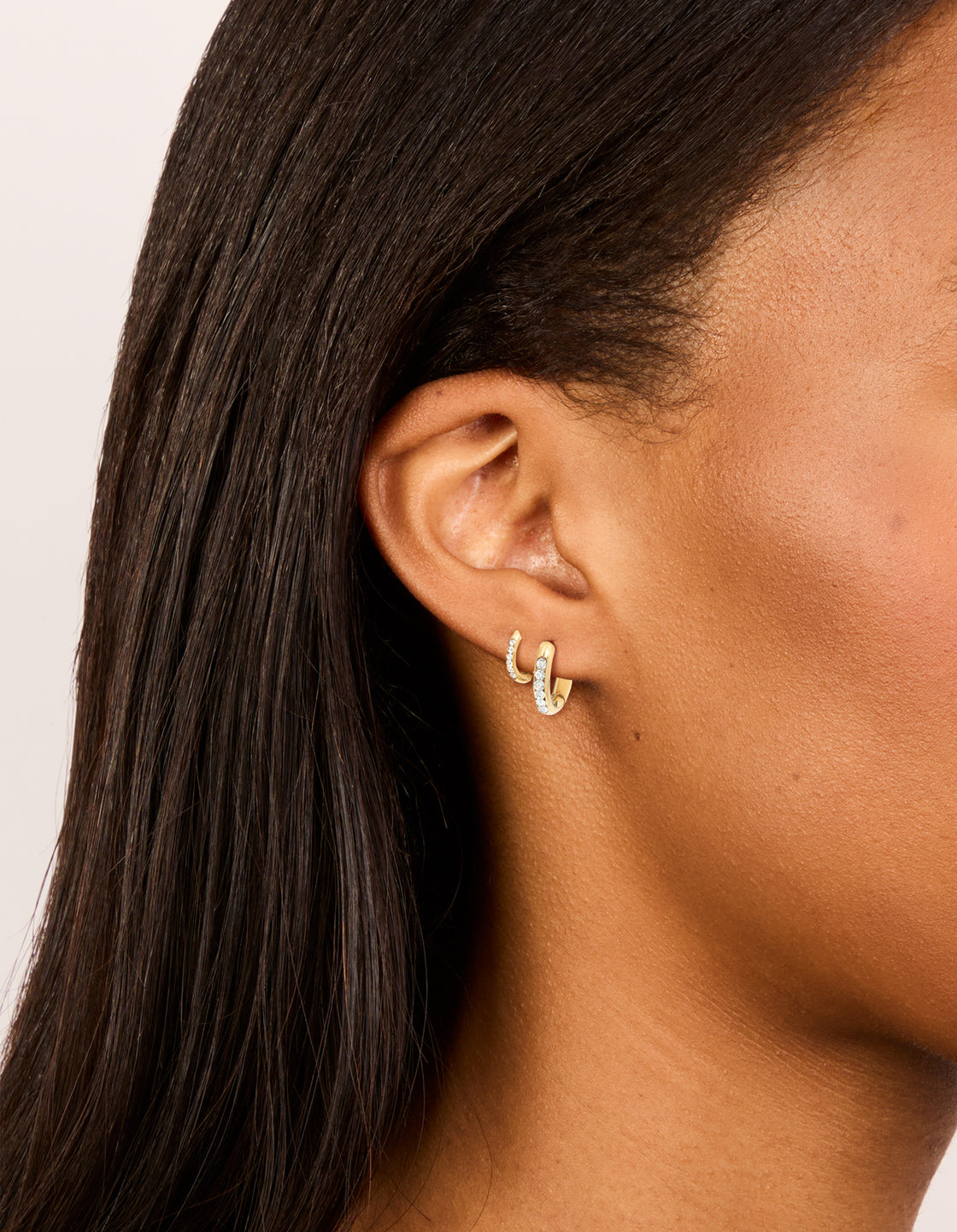 Showcasing waterproof gold plated stainless steel cubic zirconia huggie earrings in a 2-pack with crystal featuring hoop closure on ear view