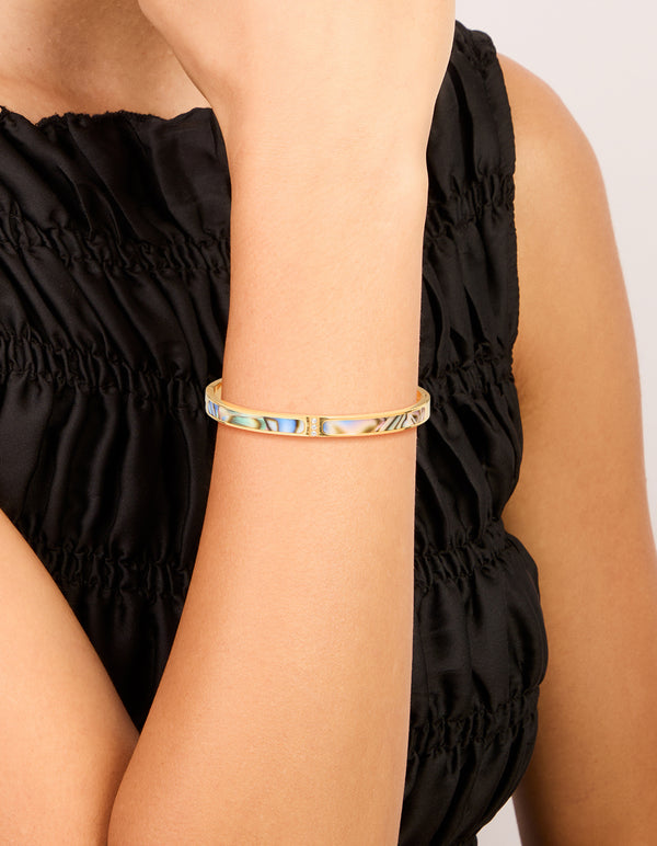 Showcasing waterproof gold plated stainless steel hinged bangle with blue and green pearlised inlay on wrist view