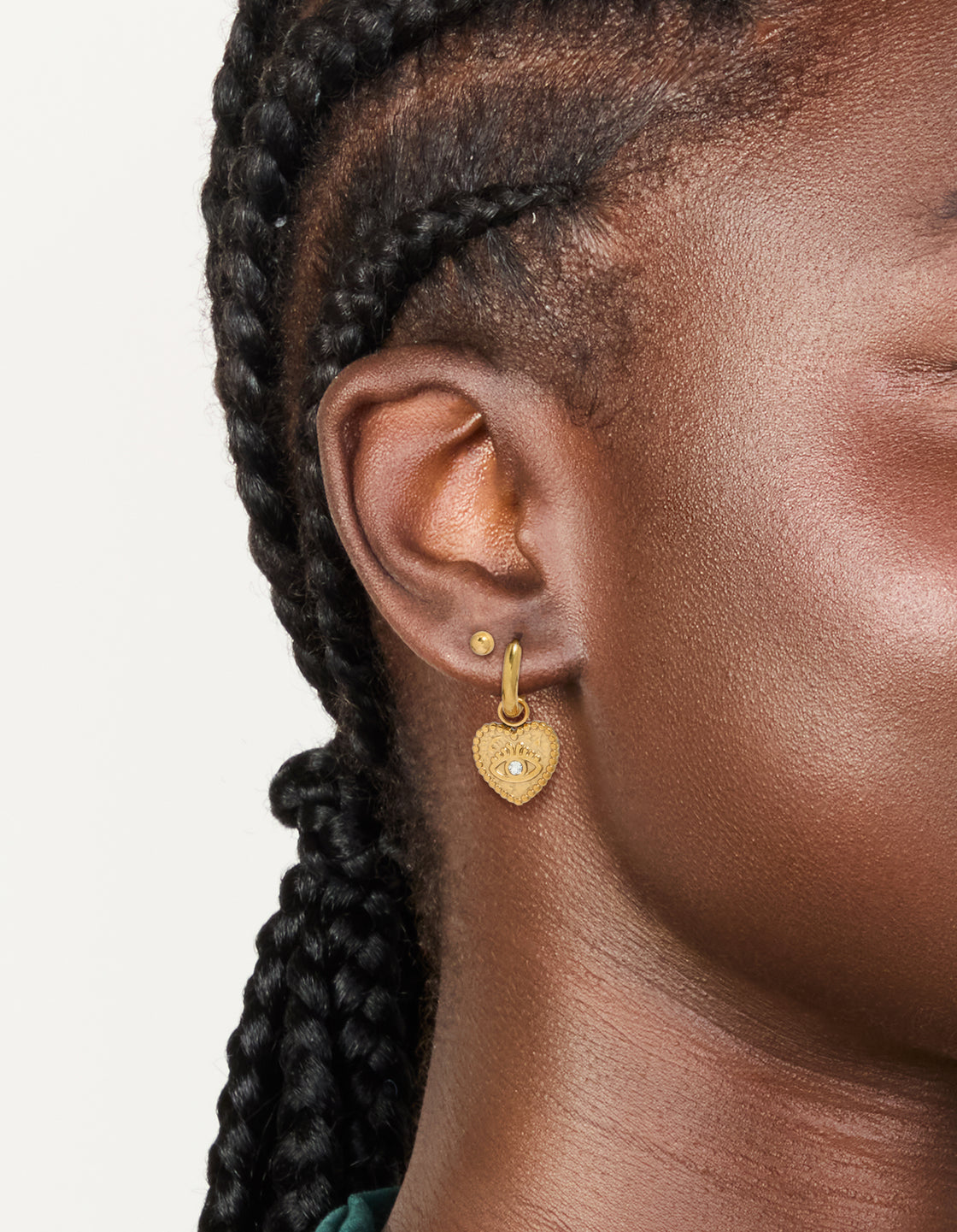Featuring waterproof gold plated stainless steel heart evil eye huggie and ball stud earrings in a 2-pack on ear view