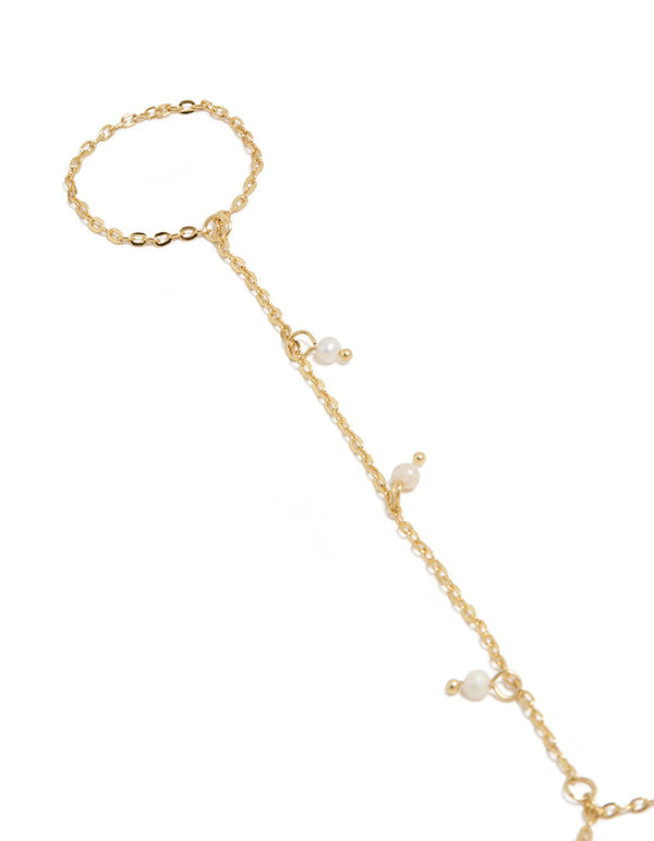 Showcasing a gold plated mini freshwater pearl droplet hand chain with charm in dainty statement style close up view