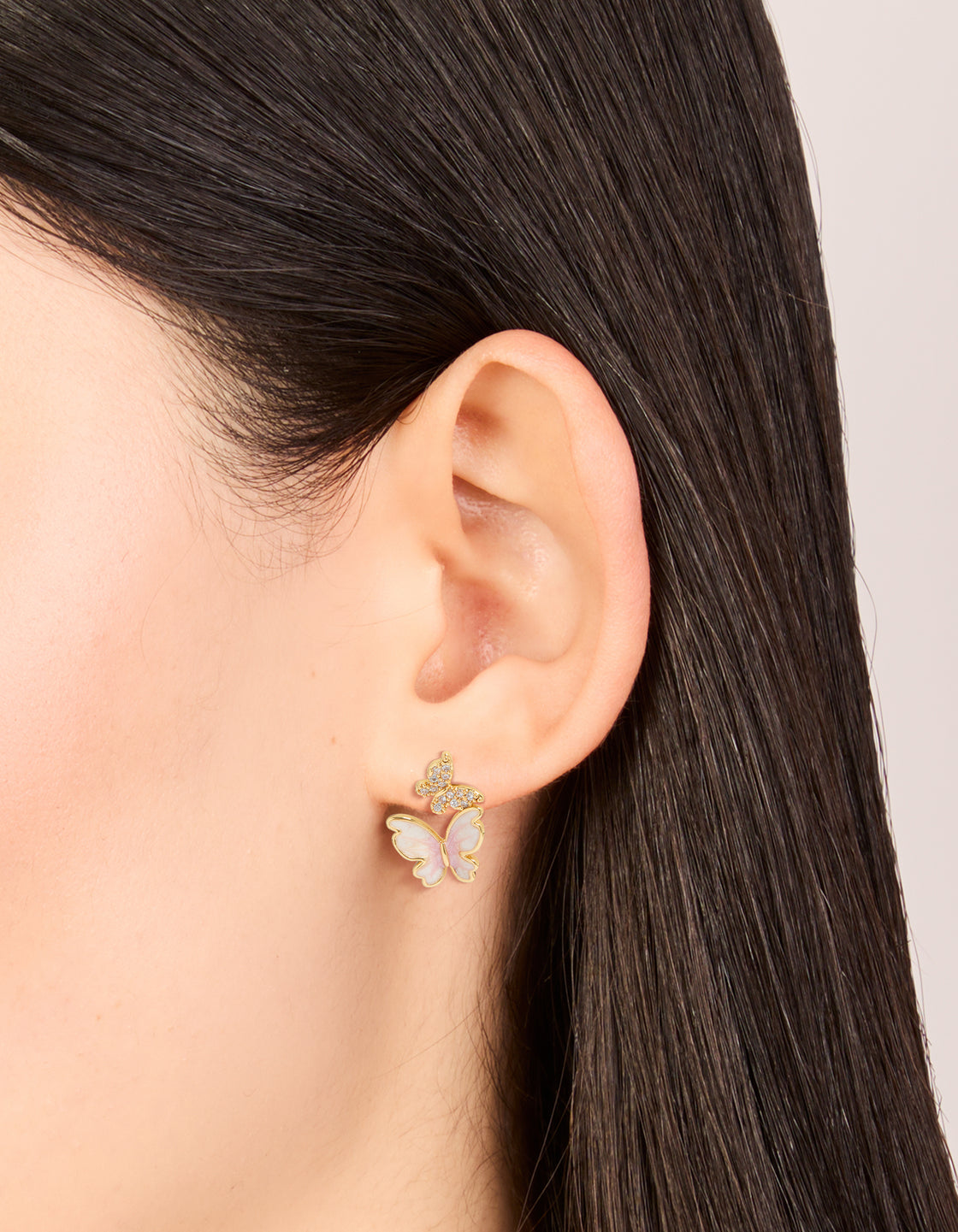 Small statement butterfly stud earrings with gold plated finish and pink enamel featuring cubic zirconia on ear view