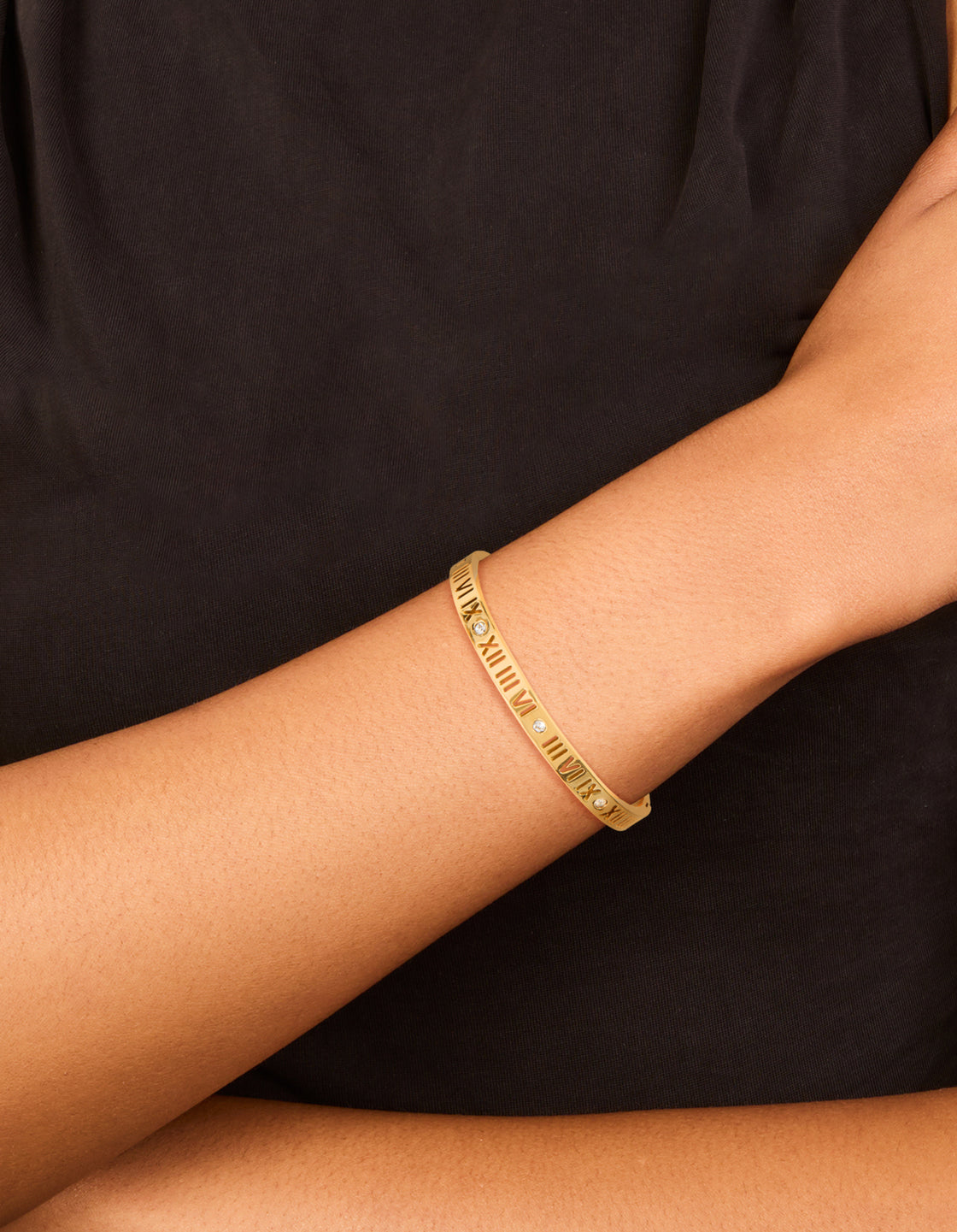 Showcasing a waterproof gold plated stainless steel bangle with roman numeral details and cubic zirconia stones on wrist view