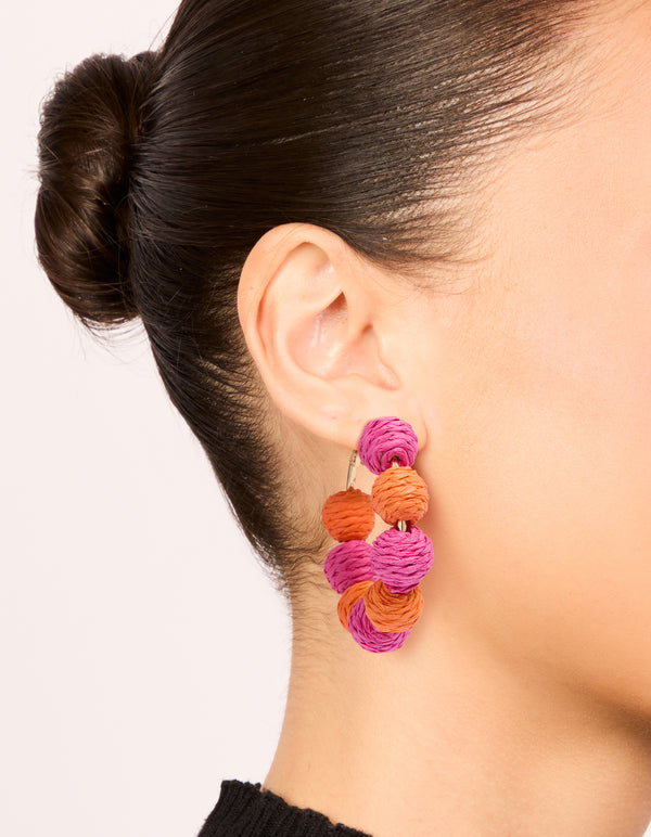 Showcasing statement hoop earrings with alternating light pink and coral paper-wrapped balls on ear view
