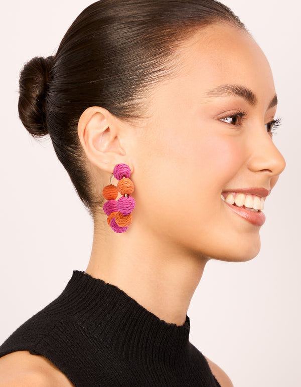 Designed with statement hoop earrings featuring alternating light pink and coral paper-wrapped balls on model view