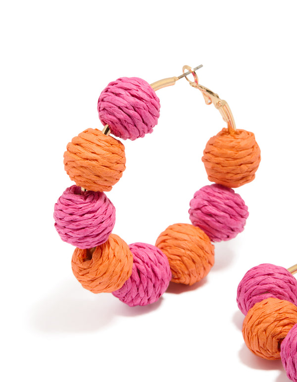 Highlighting statement hoop earrings with alternating light pink and coral paper-wrapped balls close up view