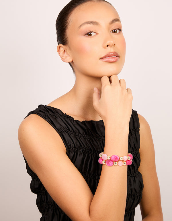 Designed with hot pink and light pink acrylic beads featuring gold accents in a 2-pack stretch bracelet set on model view