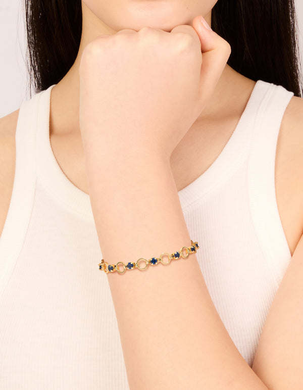 Showcasing a gold plated blue cubic zirconia alternating round link bracelet with stone cut details on wrist view