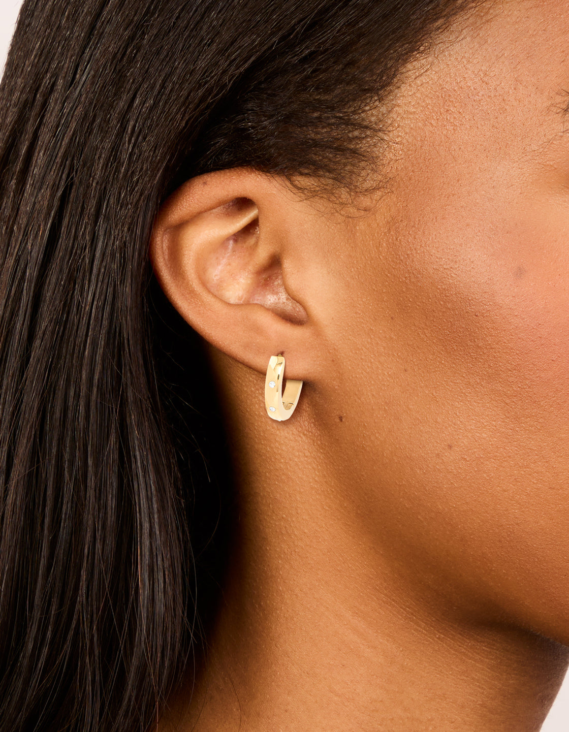 Showcasing waterproof gold plated stainless steel cubic zirconia trio huggie earrings with clear accents on ear view