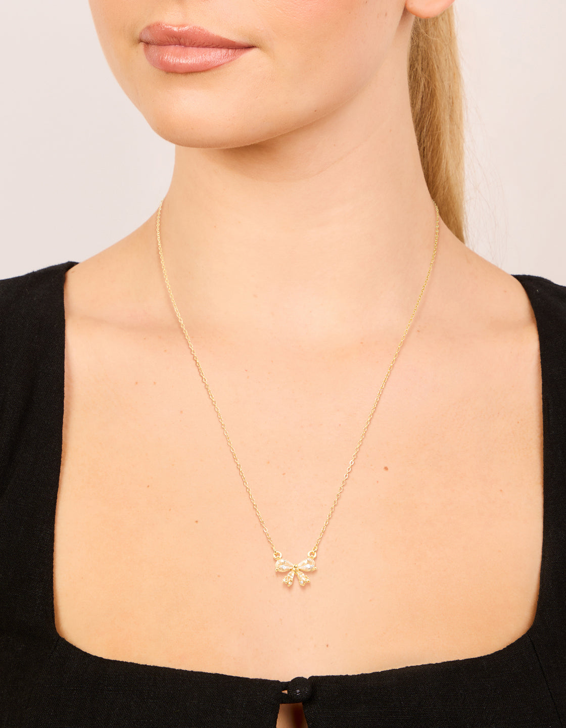 Showcasing a waterproof bow pendant necklace crafted from stainless steel with cubic zirconia in gold plated finish on neck view