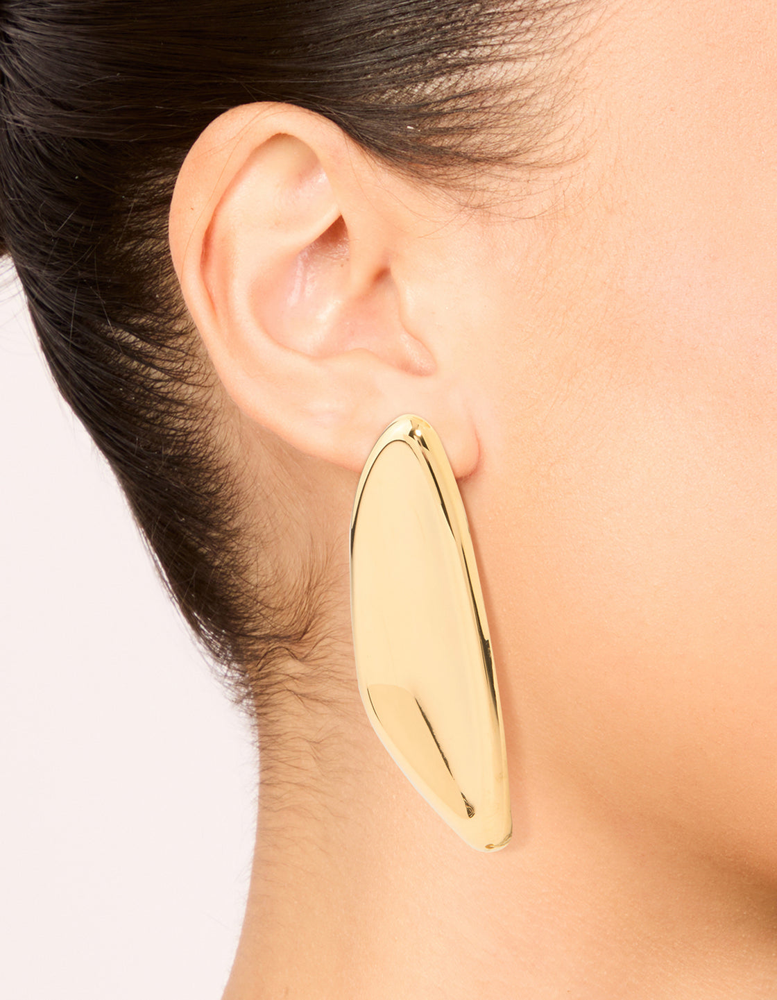 Featuring waterproof stainless steel shield stud earrings in gold plated finish on ear view