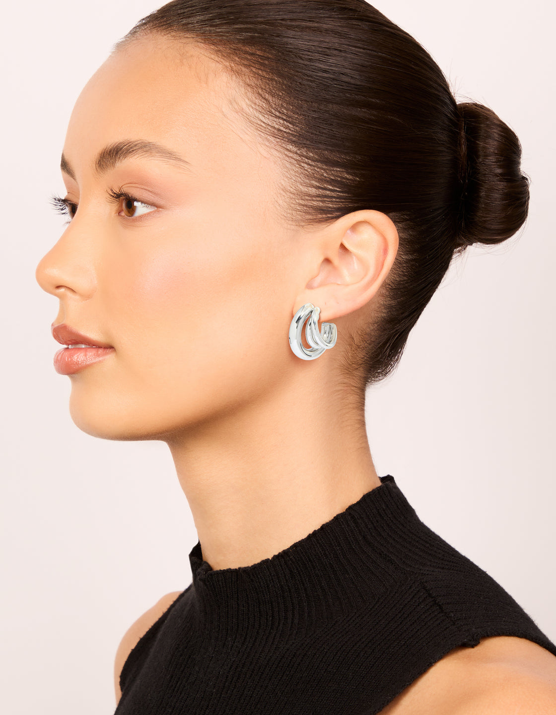 Displaying waterproof gold plated stainless steel triple illusion hoop earrings with statement styling in silver on model view