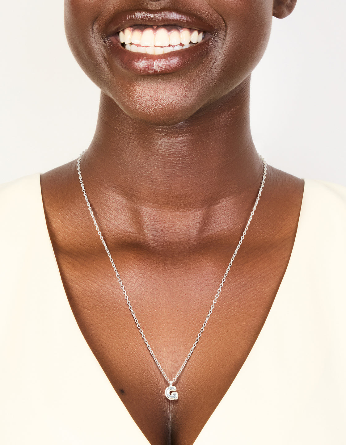 Featuring a waterproof stainless steel mini bubble letter G necklace with charm initials pendant in silver on neck view