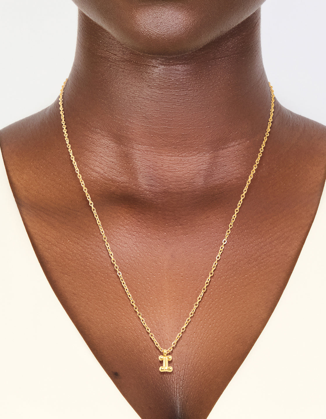 Showcasing a waterproof mini bubble letter I necklace with initial pendant in stainless steel gold plated finish on neck view