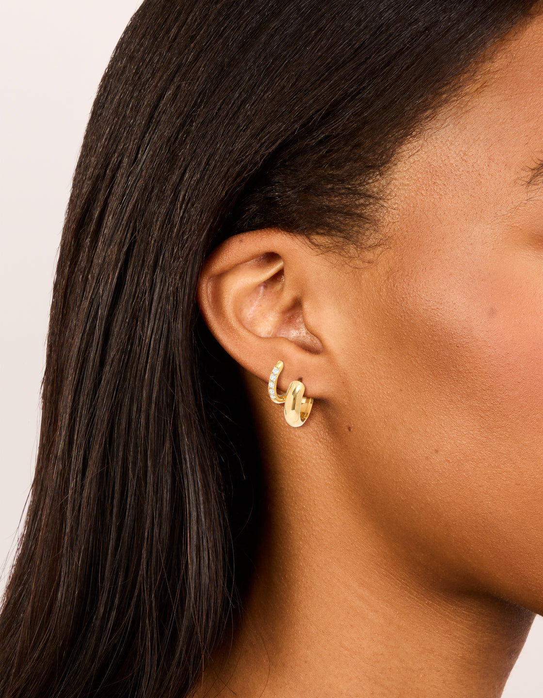 Showcasing waterproof gold plated stainless steel cubic zirconia chubby huggie earrings in a 2-pack with chunky styling and crystal accents in ear view