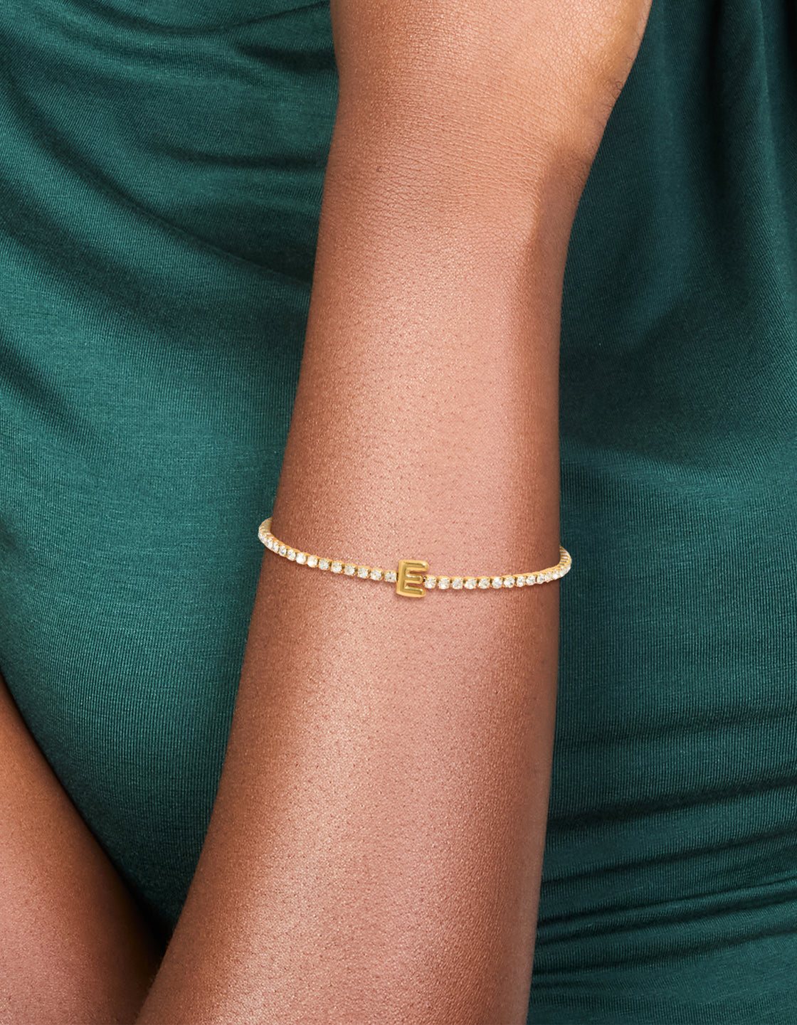 This waterproof tennis bracelet features an initial letter E, crafted from gold plated stainless steel and set with cubic zirconia on wrist view