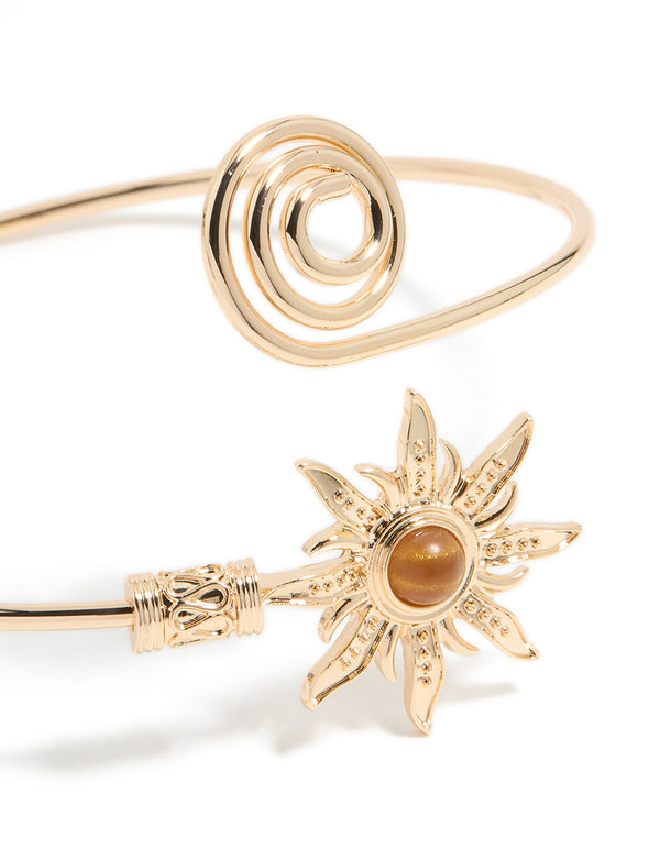 Crafted with celestial sun detailing and a swirl design, this gold statement cuff is shown in close up view