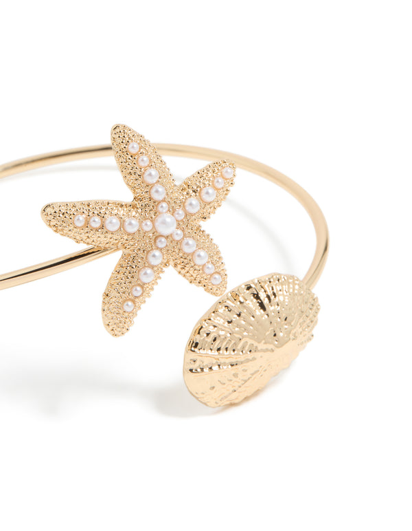 Showcasing a gold shell and pearl starfish arm cuff with ocean-inspired close up view