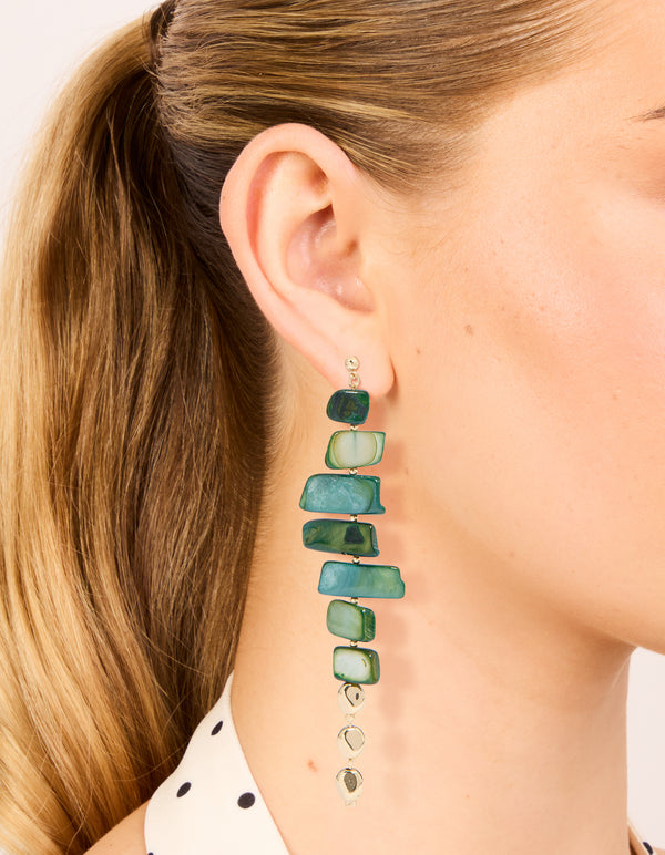 Showcasing dark green acrylic irregular shaped drop earrings featuring beads in teal and pale green with gold accents on ear view