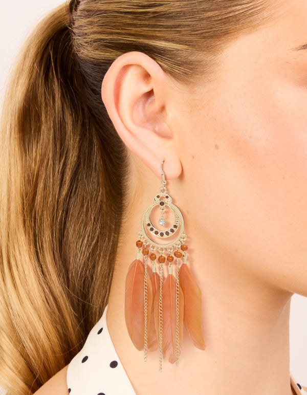 Crafted from gold featuring beads and feathers in coral, these statement drop earrings shown in on ear view