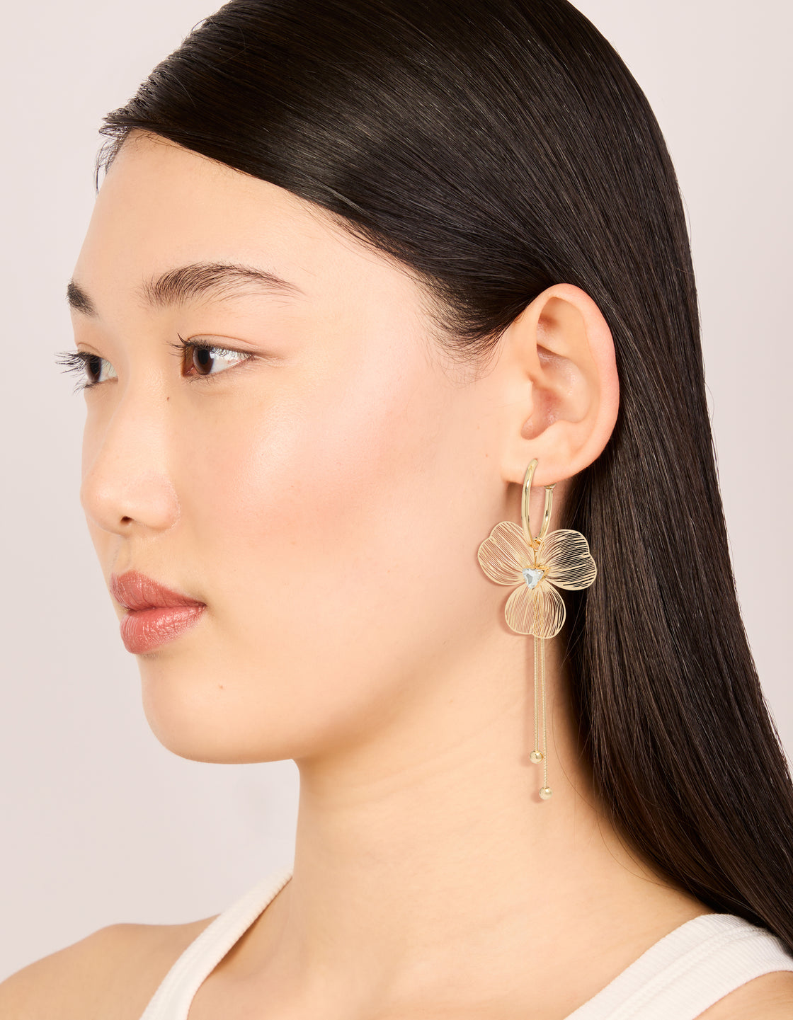 Designed with gold laser cut flower drop earrings featuring floral pattern, tassel and white gemstone charm details in statement style on model view