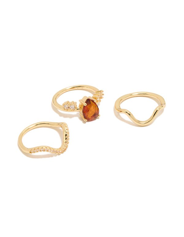 Showcasing statement wavy rings in a 3-pack featuring red teardrop cubic zirconia, crystal accents, and gold plated finish front view