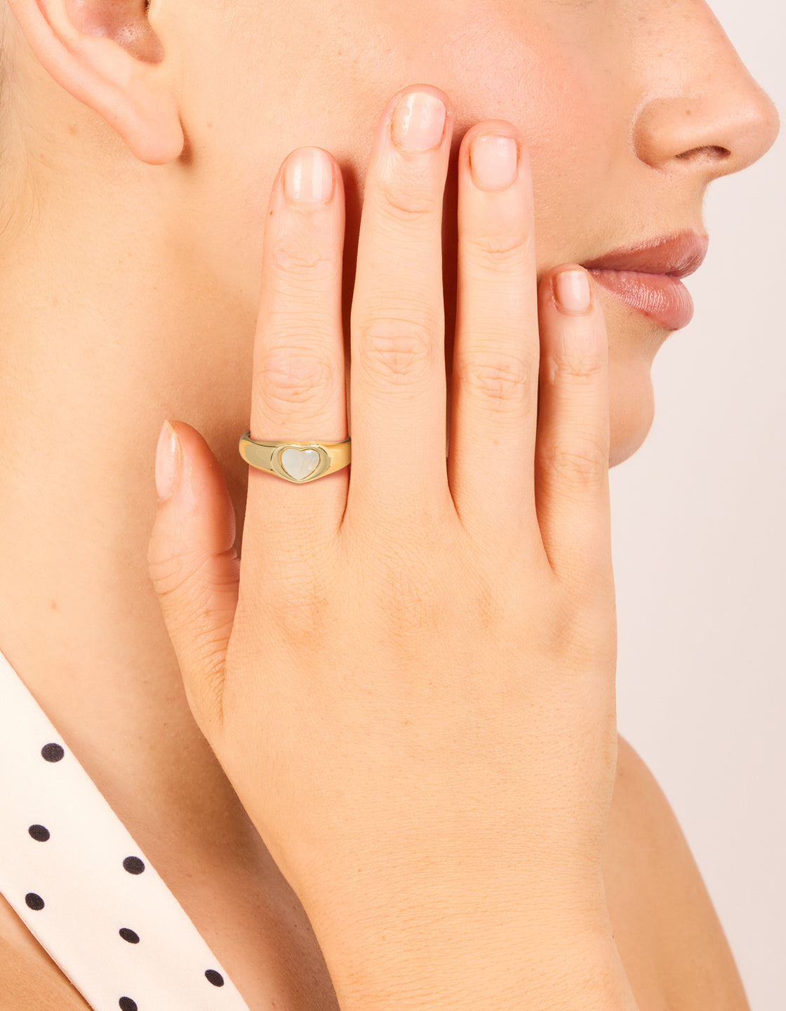 Showcasing gold plated stainless steel dainty heart signet ring with white inlay and waterproof material on finger view