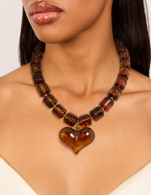 Featuring a brown square bead and heart necklace with statement design in gold tones on neck view