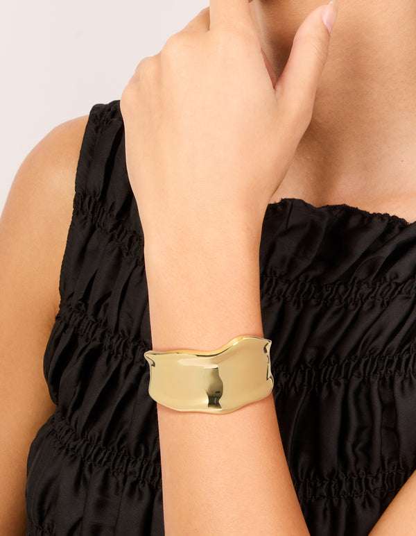 Showcasing a statement wavy wrist cuff crafted from plated metal in gold bangle on wrist view