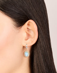 Featuring gold plated blue cubic zirconia oval halo drop earrings worn on ear to display scale and placement on ear view - link has visual effect only